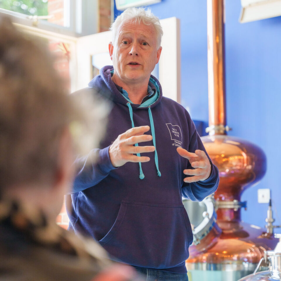 The distiller talking residents through the process beside the copper still